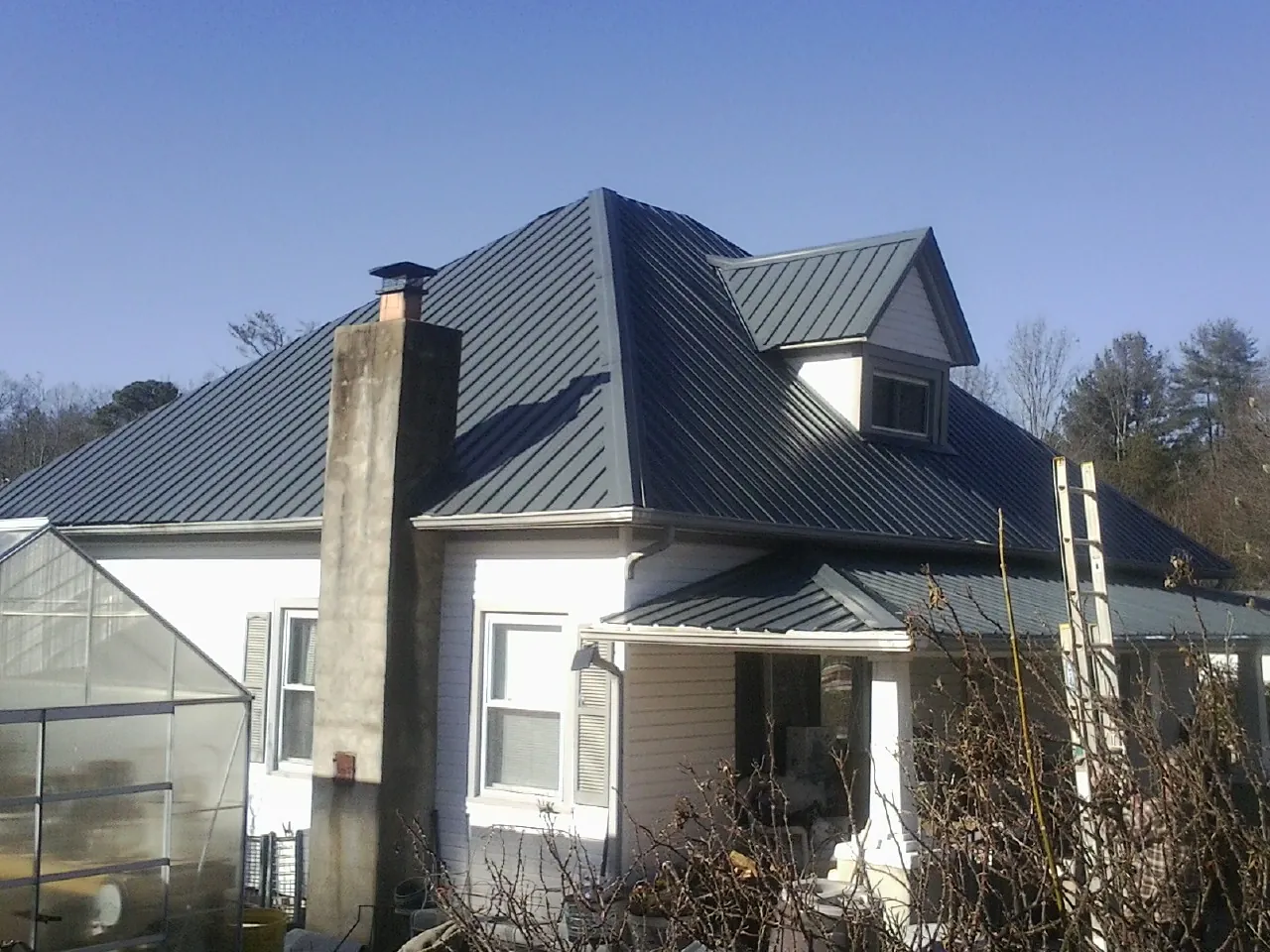 Dark blue standing seam metal roof on a white farmhouse with dormer — Slate & Tile Roof Repair by Roofing Brothers in Wiota