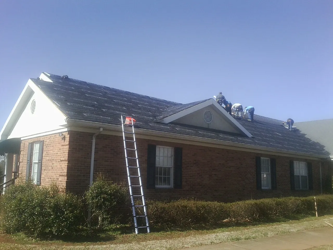 Crew tearing shingles off a brick ranch roof with a ladder set — Metal Roof Repair work by our crew in Wiota