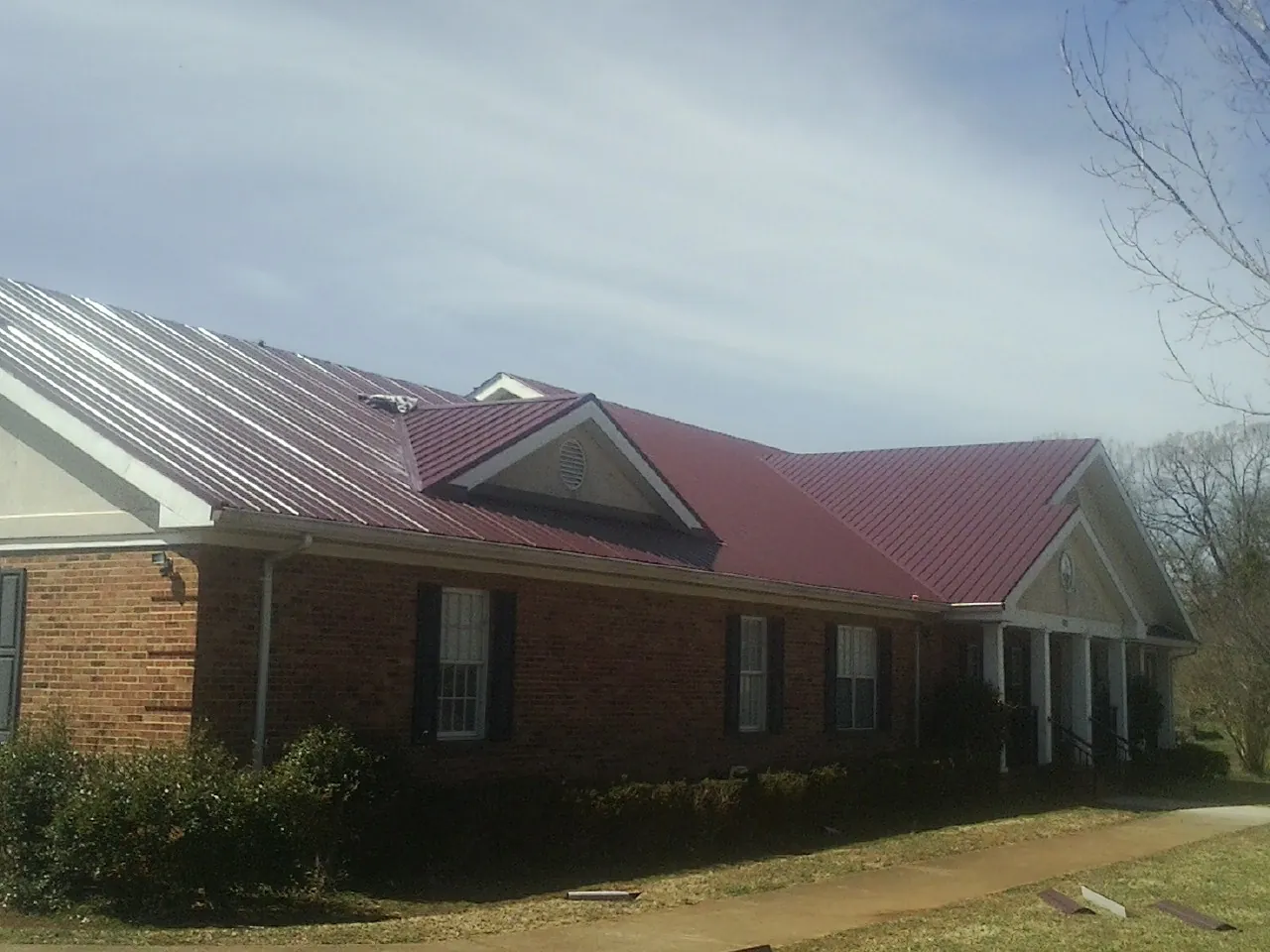 Red metal roof with gabled entries on a long brick building, from a Hail Damage Roof Repair job in Wiota