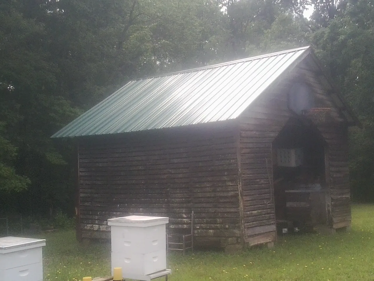 Green metal roof on a weathered barn beside stacked beehives in Wiota