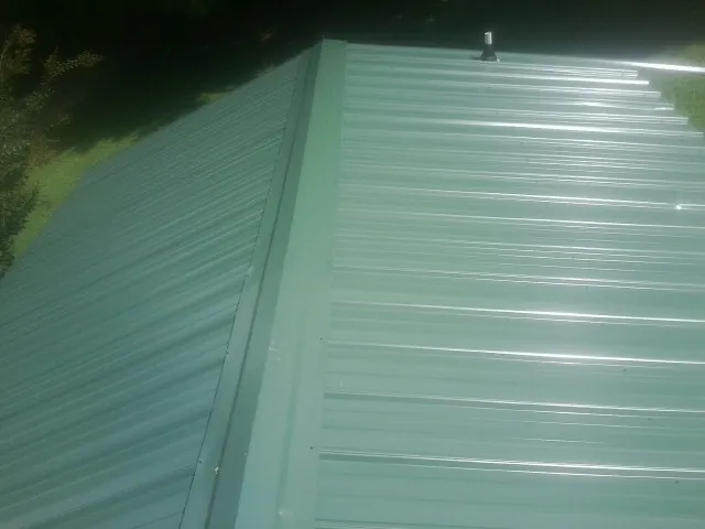 New green metal panels meeting at the ridge of a roof — Flat Roof Repair work by our crew in Wiota