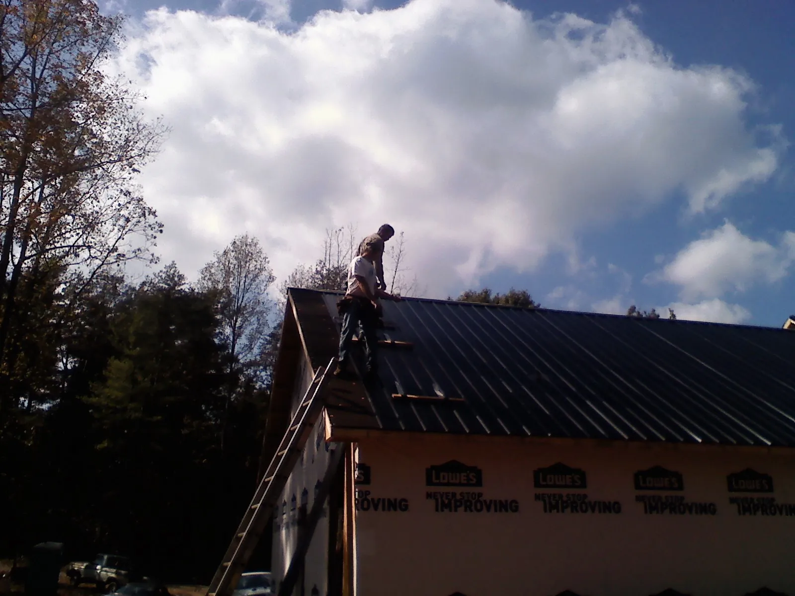 Roofer fastening dark metal panels high against a cloudy sky, from a Roof Inspection job in Wiota