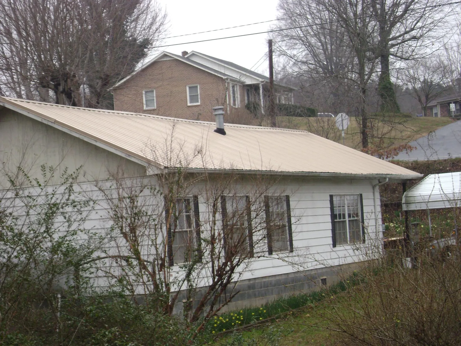 Tan metal roof on a white sided house set into a hillside — Commercial Roofing by Roofing Brothers in Wiota